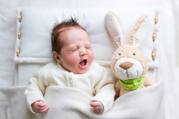 Cute yawning baby girl in а crib with a toy rabbit